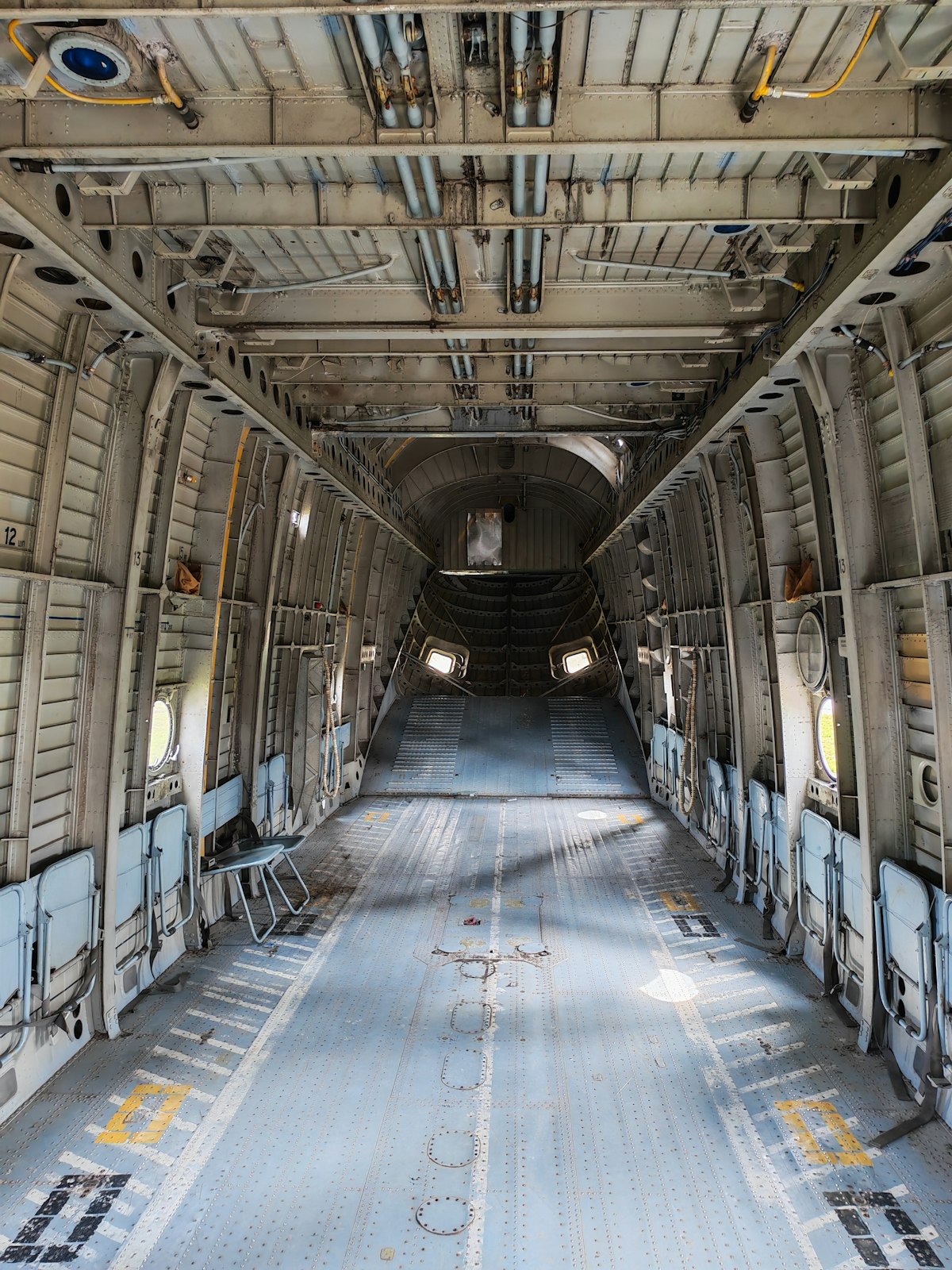 Interior of a military cargo aircraft hold showing the empty cargo bay floor, tie-down rings, and overhead systems that loadmasters manage during operations